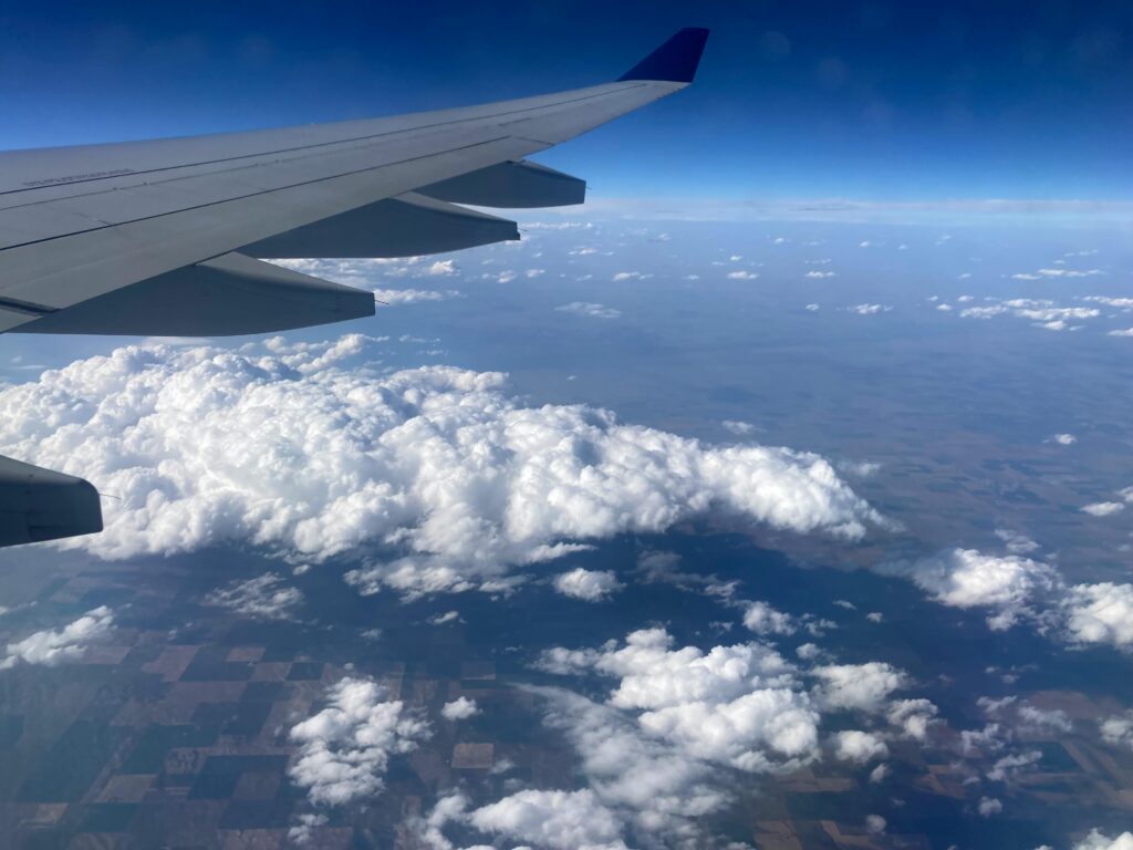 Scenic aerial view from an airplane wing showing clouds and farmland below.